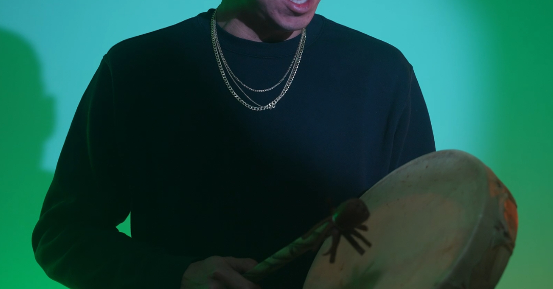 A man with a drum stands in front of a striking green light