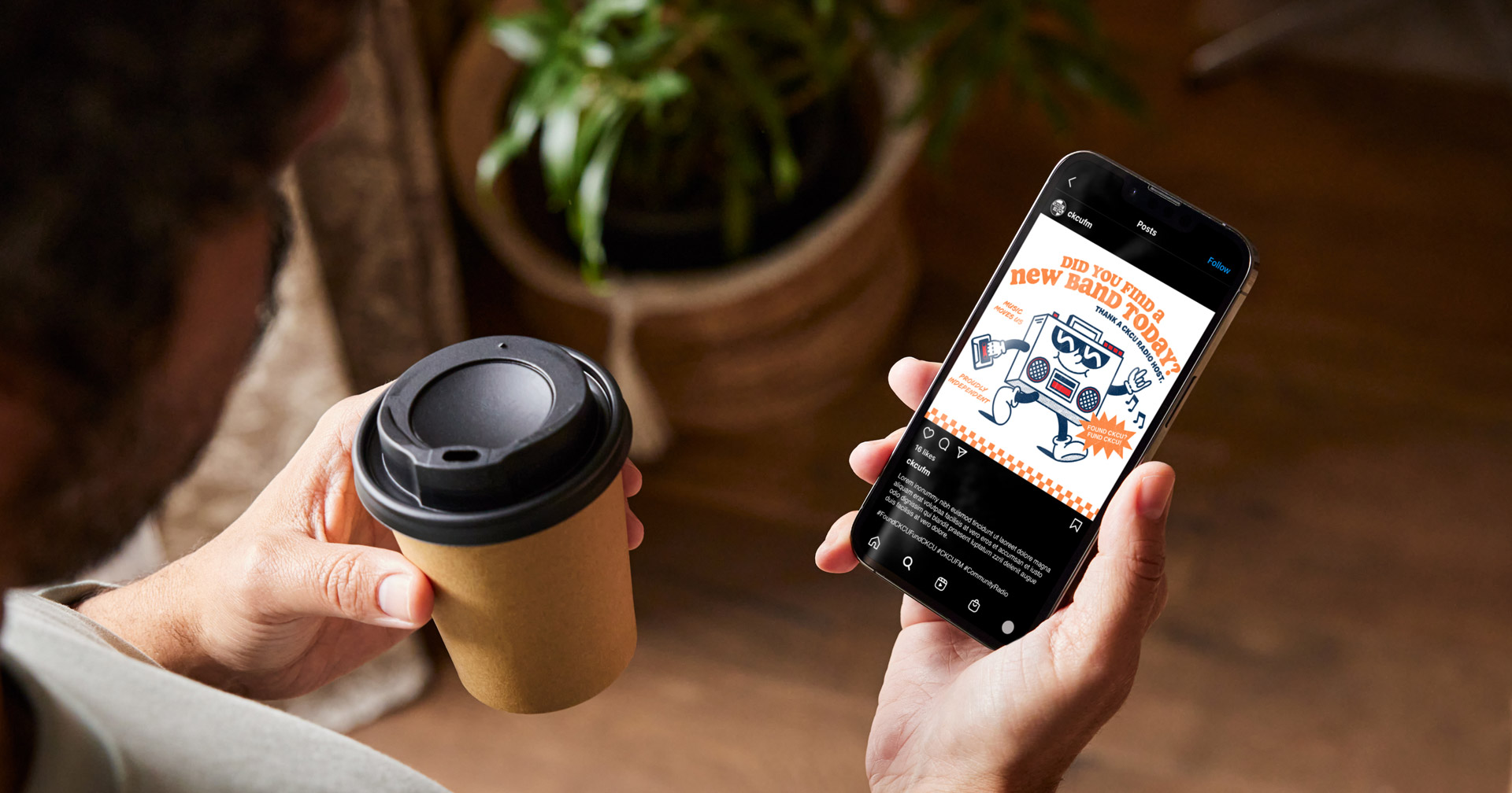A person holding a coffee cup looks at a smartphone displaying a colorful cartoon advertisement about bathroom upgrades, with a plant and basket visible in the background.