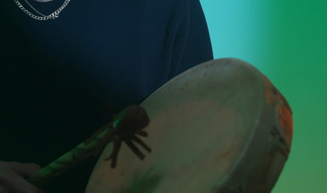 A man with a drum stands in front of a striking green light
