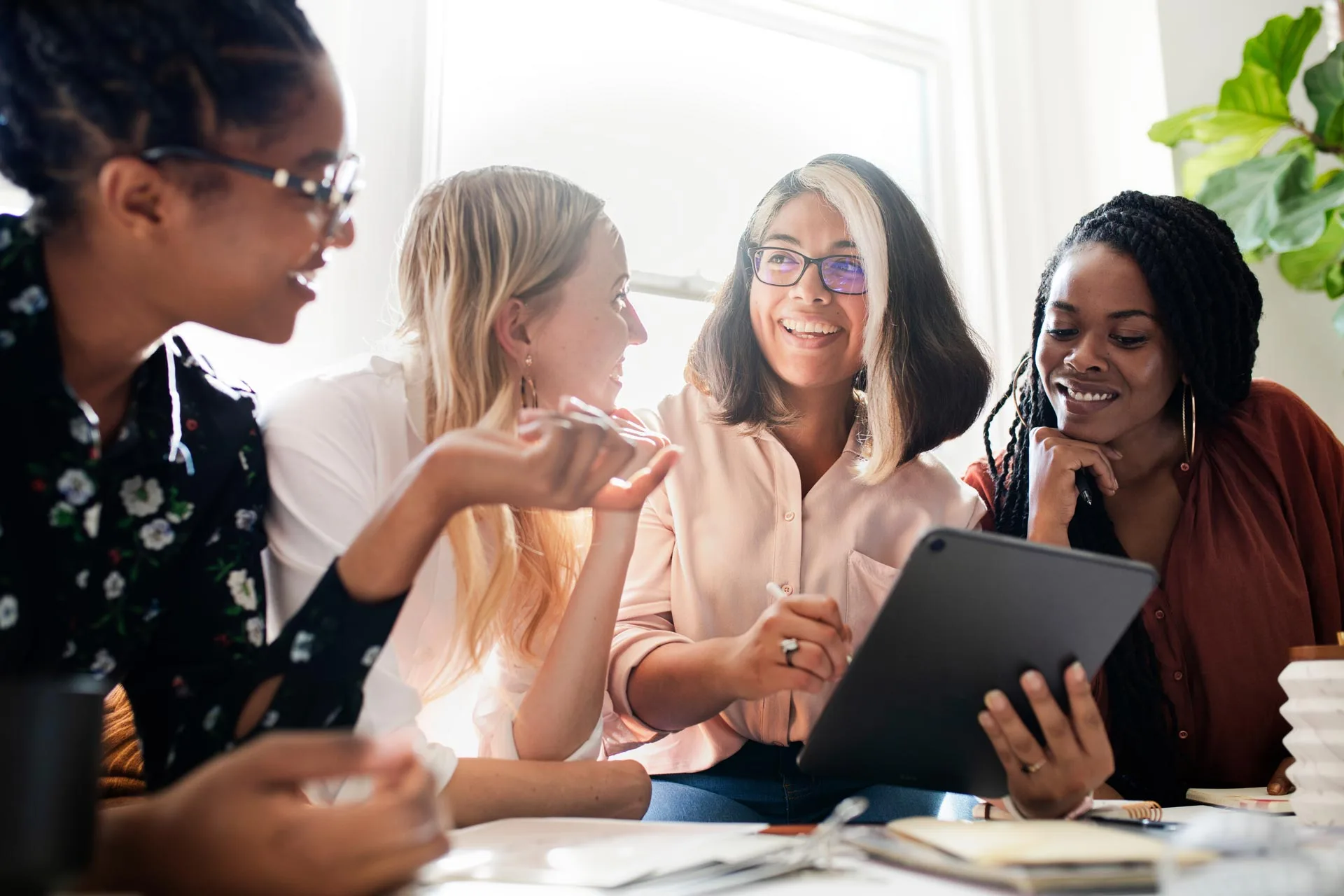 Four women sitting around a table, looking at a tablet.