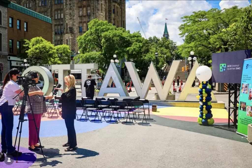 A group of people gathered around a large sign displaying the word "Ottawa."