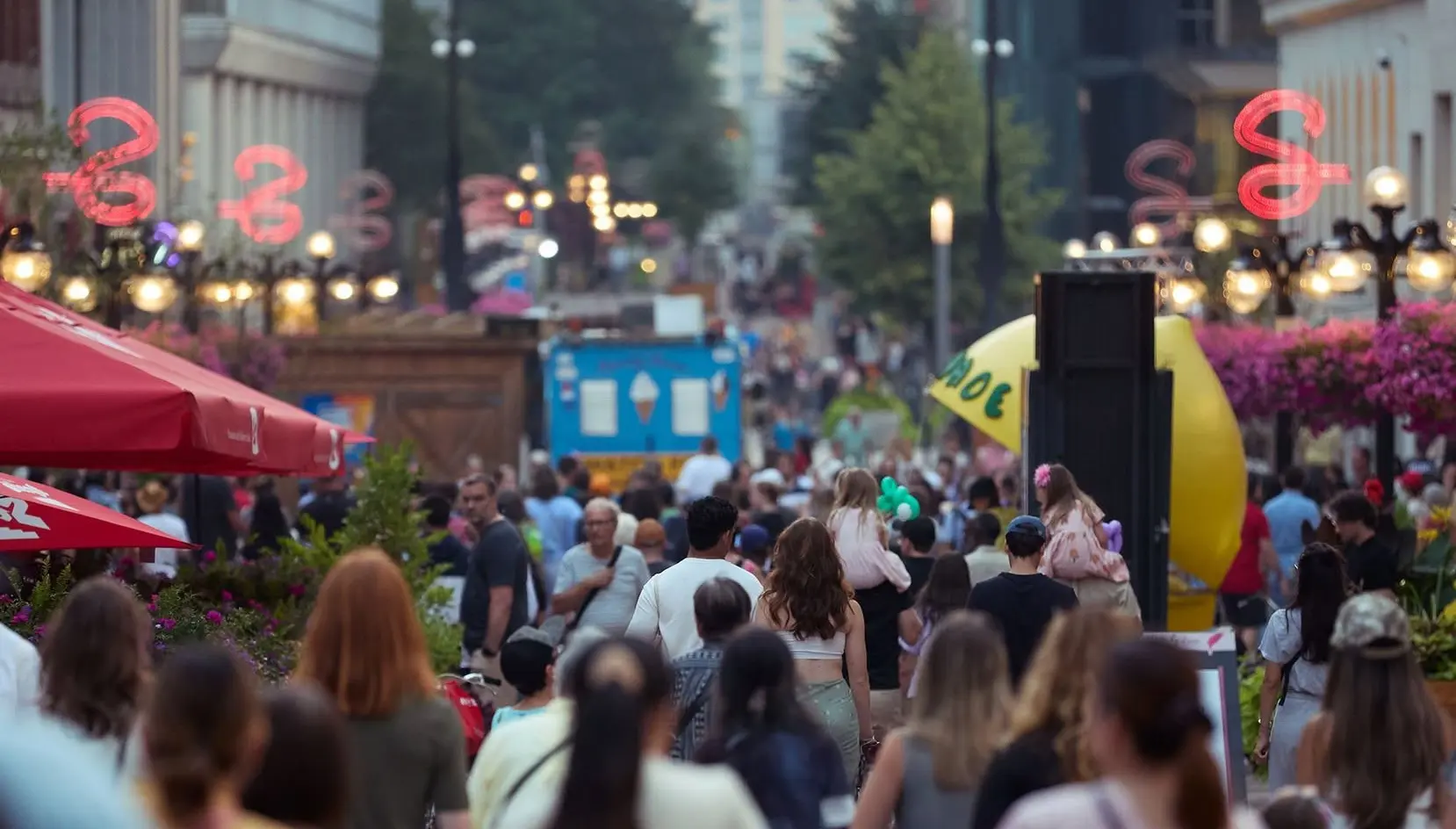 A lively urban scene featuring a crowd of people walking and dining along a busy street